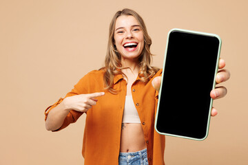 Young amazed woman wear orange shirt casual clothes hold in hand use point finger on blank screen...