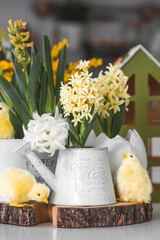 Happy Easter. Spring yellow hyacinth flowers in an egg-shaped vase, chicken chicks on a white table. In the background is a white Scandinavian-style kitchen. Easter decor in the house.