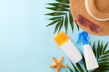 Summer Skincare Essentials: Top view shot of sunscreen spray, straw hat, pink sunglasses, and tropical leaves on a light blue background with space for messages