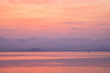 Fototapeta na wymiar Serene twilight hues reflect off a tranquil lake, with distant mountains shrouded in mist.