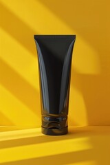 A tube of black cream on a bright yellow surface, ideal for beauty or skincare product concepts