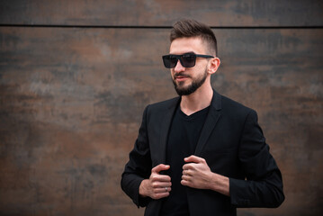 Confident and handsome. Young man wearing black suit and sunglasses isolated on the bacground.