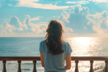 Fototapeta premium Woman standing on balcony overlooking the ocean. Suitable for travel and relaxation concepts