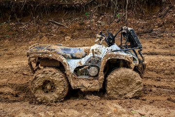 Fototapeta na wymiar Quad bike in mountainous area and impenetrable road in dense forest. The ATV is very much covered with mud