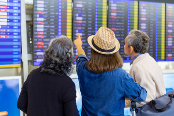 Group of Asian family tourist passenger with senior parent looking at the departure table at airport terminal for airline travel and holiday vacation concept