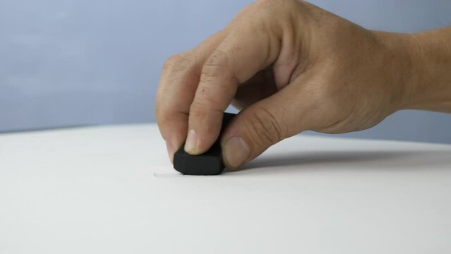 Hand holding black eraser scrap on paper background. 
Error Eraser dust delete wrong words on white background.
top view.   Slow motion.