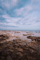 Sea view with rocky beach and sky with clouds, vertical