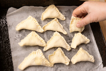 Pies for baking are laid out on a baking sheet with parchment. Cooking pies.