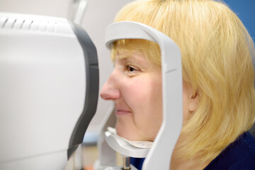 Portrait of mature woman during visit to optometrist for microscopic analysis of eyelids, sclera,...