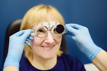 Smiling senior woman wearing optometrist trial frame at ophthalmology clinic. Appointment by...