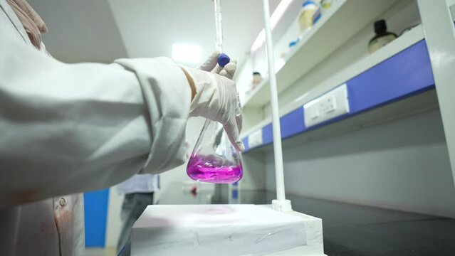 Scientist doing science experiment in a beaker. flask titration with colorful pink chemical liquid in a laboratory with science lab equipments	