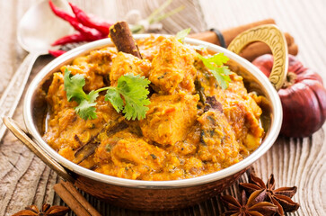 Traditional Indian chicken curry served with spices and chicken pieces as close-up in a kadai bowl