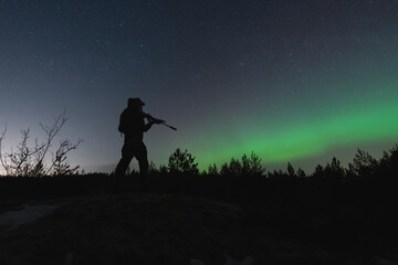 A military soldier with a night vision device and a rifle with a suppressor in the forest against...