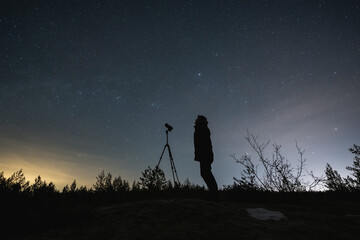 Man landscape astrophotographer with a camera on a tripod outdoors in early spring at night under...