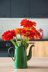 Bouquet of red zinnia in a vintage green coffee pot on a wooden table in a kitchen