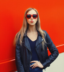 Portrait of beautiful stylish blonde young woman model blowing kiss in red heart shaped sunglasses
