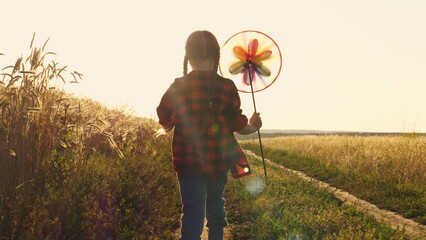 Little child girl plays with her toy windmill park sunset. child kid baby silhouette running girl...