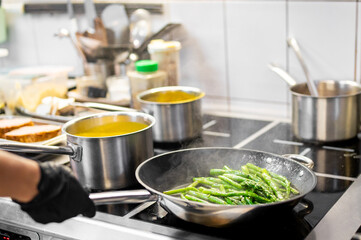 A chef sautéing green beans in a professional kitchen. Pots of soup simmer on the stove. Modern culinary workspace