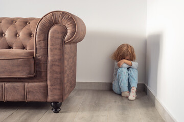 A child is sitting on the floor, next to a leather sofa. The child is crying and he is upset....