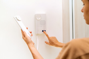 Using intercom at home. Woman uses intercommunication device at her apartment. Using intercom at...