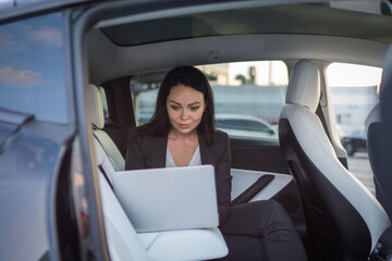 Beautiful businesswoman using laptop while sitting on back seat in the car while working online. Business, people, distance work concept