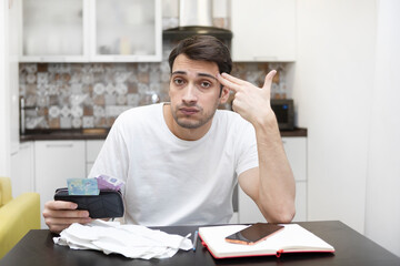 Close up of unhappy man sitting at the table, stressed and confused by calculate expense from invoice or bills, have no money to pay mortgage or loan. High prices and spending money concept