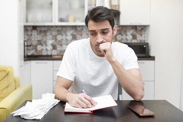 Close up of unhappy man sitting at the table, stressed and confused by calculate expense from invoice or bills, have no money to pay mortgage or loan. High prices and spending money concept