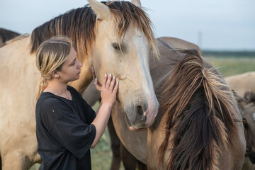 A young beautiful blonde girl plays with a horse on the field.
