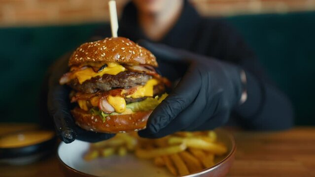 a person wearing black gloves is holding a hamburger with a toothpick in their hand