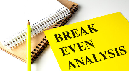 BREAK EVEN ANALYSIS text on yellow paper with notebooks