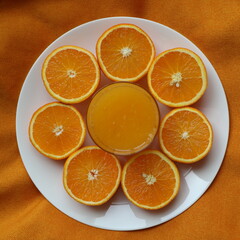 glass of orange juice  and surrounding it are sliced halves of oranges arranged