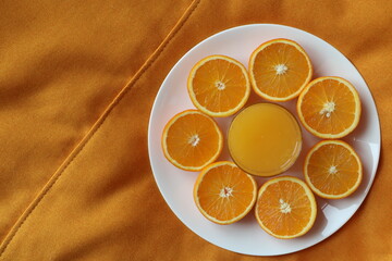 glass of orange juice  and surrounding it are sliced halves of oranges arranged on the orange textured surface