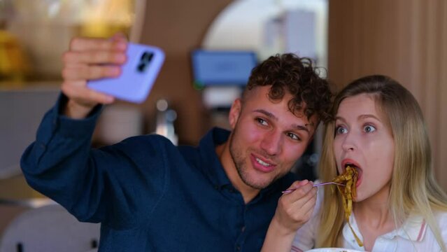 Young couple on a date taking selfie photo while eating pasta in restaurant