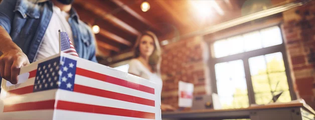 Deurstickers A woman is standing behind a box featuring an American flag. She appears to be interacting with the box in some way, possibly related to voting or patriotism. © MYDAYcontent