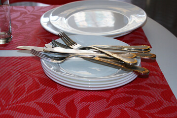 Ready white plates, forks, knives and glasses on the table. Crockery and cutlery on a red...
