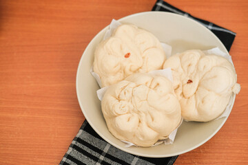 Three Bakpao / Chinese Pao in ceramic plate with black strip napkin as background on top of wooden table. Food concept.
