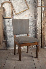 An old oak chair stands in a dirty room, on the old floor next to other vintage things