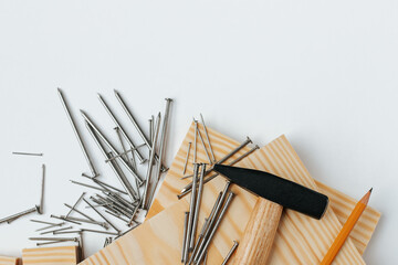 On a white background at the bottom of the frame there are two boards, on them are a hammer with nails and a pencil. nails are scattered nearby