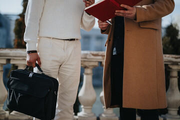 Crop of two business professionals engaging in a casual outdoor meeting, one holding a briefcase...