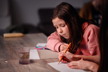 A young girl deeply engaged in drawing, with a clear expression of concentration and a water glass...