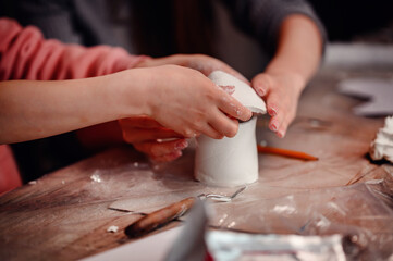 A child's hands carefully construct a clay house, with the focused guidance of a parent, symbolizing the foundational joy of building and learning together