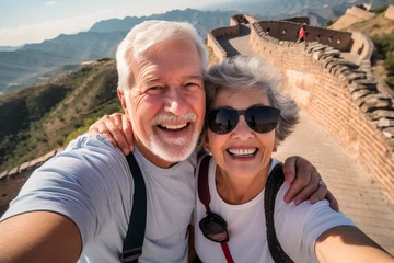 Fotobehang A happy elderly tourist couple take a selfie in China with the Great Wall in the background. Travel retirement concept. AI generated. © serperm73