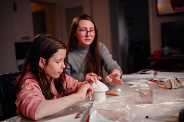 A mother watches over her daughter as she carefully sculpts with clay, a tender moment of familial...
