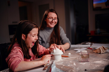The sheer delight of a girl sculpting with clay is shared with her mother, capturing the essence of...