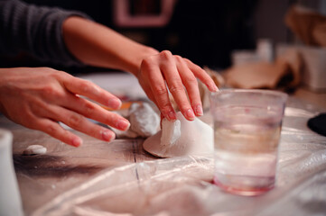 A child's hands carefully construct a clay house, with the focused guidance of a parent, symbolizing the foundational joy of building and learning together