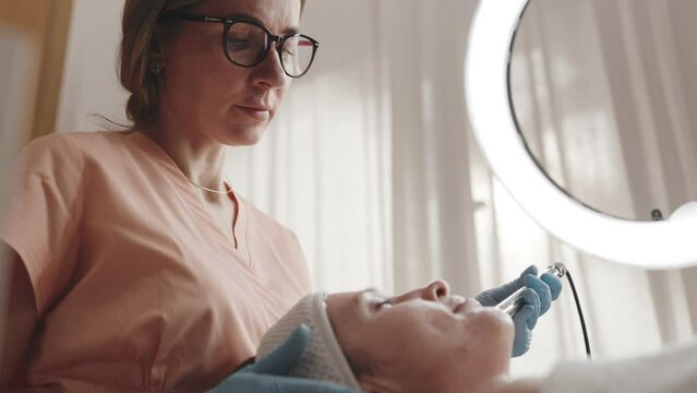 Close-up of a focused aesthetician giving a client a non-invasive microcurrent facial therapy in a modern beauty clinic.