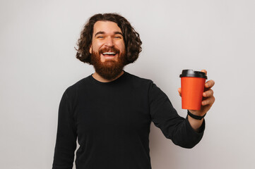 Cheerful bearded man is holding a red paper take away cup over white background.