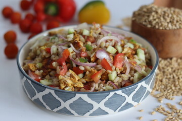 Hulled barley chicken salad. Hearty salad with hulled barley, chicken, cucumber, tomato, onions in a ceramic bowl