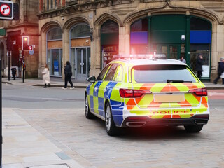 Police car parked on quiet English city street with rear red flashing lights