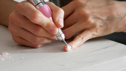 Close-up of a girl's hands removing an old layer of gel polish from a nail using a manicure machine